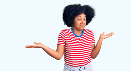 Young african american girl wearing casual clothes clueless and confused expression with arms and...