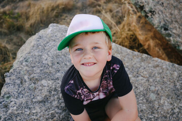Little boy sitting on rock smiling up at camera