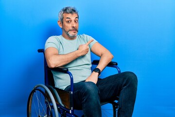Fototapeta na wymiar Handsome middle age man with grey hair sitting on wheelchair pointing aside worried and nervous with forefinger, concerned and surprised expression