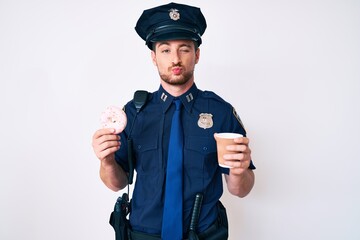Young caucasian man wearing police uniform holding take away coffee and donut looking at the camera blowing a kiss being lovely and sexy. love expression.