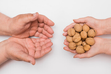 Hands of an elderly woman pass a bunch of whole walnuts into the hands of an elderly man isolated on white background. Care and attention concept