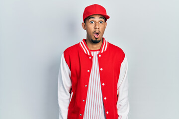 Young african american man wearing baseball uniform afraid and shocked with surprise expression, fear and excited face.