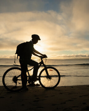 Silhouette image of a cyclist getting ready to ride on the beach at sunrise. Vertical format.