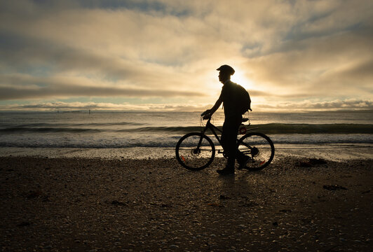 Silhouette image of a cyclist walking and pushing the bike on the beach at sunrise