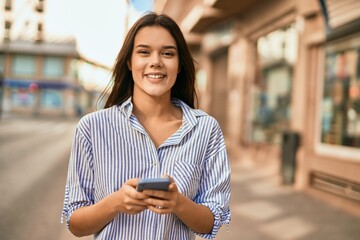 Young hispanic girl smiling happy using smartphone at the city.