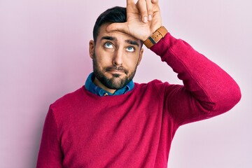 Young hispanic man wearing casual clothes making fun of people with fingers on forehead doing loser gesture mocking and insulting.