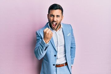 Young hispanic businessman wearing business jacket angry and mad raising fist frustrated and furious while shouting with anger. rage and aggressive concept.