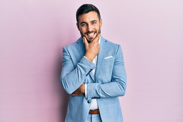 Young hispanic businessman wearing business jacket looking confident at the camera smiling with crossed arms and hand raised on chin. thinking positive.