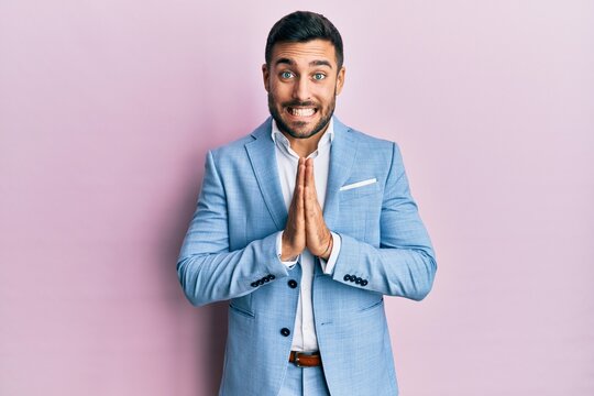 Young hispanic businessman wearing business jacket praying with hands together asking for forgiveness smiling confident.