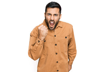 Young hispanic man wearing casual clothes angry and mad raising fist frustrated and furious while shouting with anger. rage and aggressive concept.