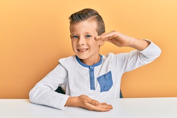 Naklejka premium Adorable caucasian kid wearing casual clothes sitting on the table gesturing with hands showing big and large size sign, measure symbol. smiling looking at the camera. measuring concept.