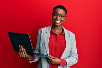 Young african american woman holding laptop looking positive and happy standing and smiling with a confident smile showing teeth