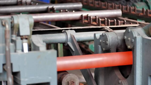 The process of manufacturing steel pipes in a steelwork, close-up of machine transporting hot steel pipes