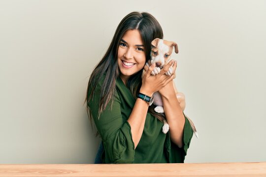 Young hispanic girl smiling happy and hugging dog sitting on the table over isolated white background.