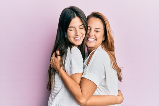 Beautiful hispanic mother and daughter smiling happy hugging over isolated pink background.