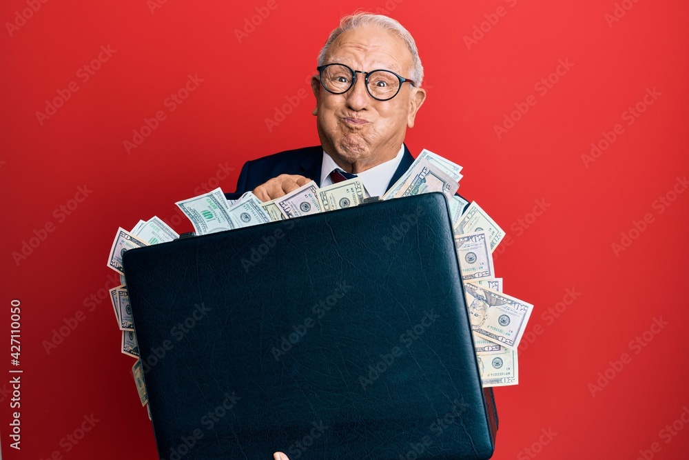 Canvas Prints senior caucasian man holding briefcase full of dollars puffing cheeks with funny face. mouth inflate