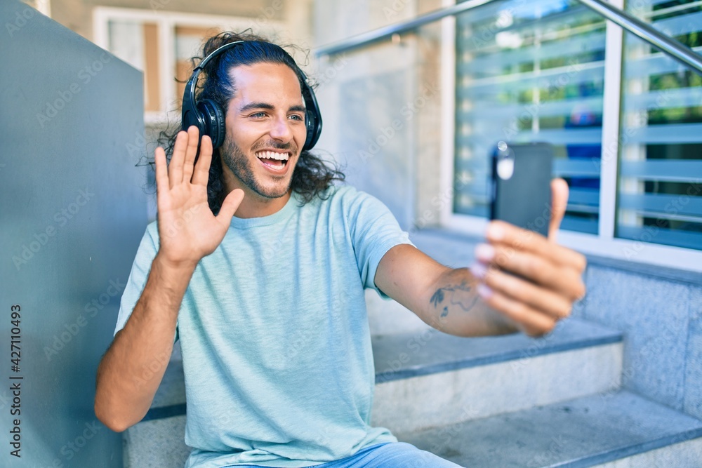 Wall mural Young hispanic man smiling happy doing smartphone video call at city.