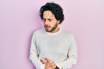 Handsome hispanic man wearing casual white sweater with hand on stomach because indigestion, painful illness feeling unwell. ache concept.