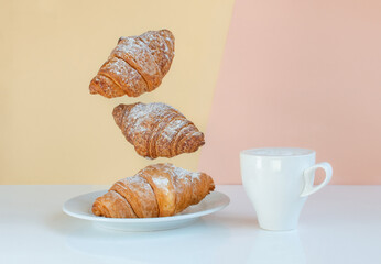 Levitating food, time to wake up call. Flying croissants for breakfast and a cup of coffee, cocao or milk on a beige background color sunrise. Modern breakfast still life concept food.