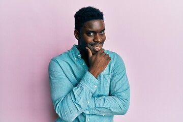 Handsome black man wearing casual clothes looking confident at the camera smiling with crossed arms and hand raised on chin. thinking positive.