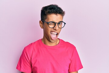 Young handsome african american man wearing glasses over pink background winking looking at the camera with sexy expression, cheerful and happy face.