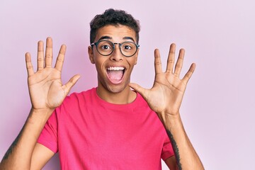 Naklejka premium Young handsome african american man wearing glasses over pink background showing and pointing up with fingers number ten while smiling confident and happy.