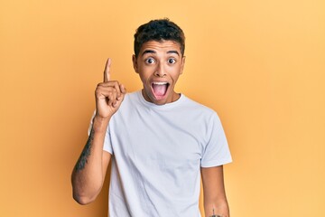 Young handsome african american man wearing casual white tshirt pointing finger up with successful...
