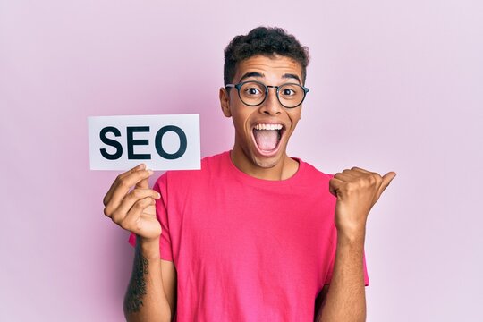 Young handsome african american man holding seo message paper pointing thumb up to the side smiling happy with open mouth