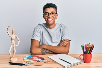 Young handsome african american man painter sitting palette and art manikin happy face smiling with...