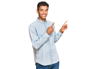 Young handsome african american man wearing casual clothes smiling and looking at the camera pointing with two hands and fingers to the side.