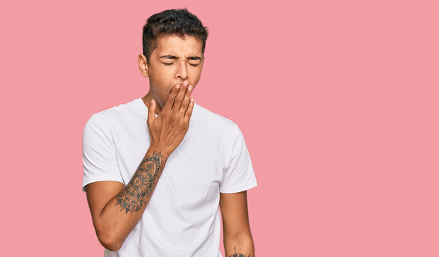 Young handsome african american man wearing casual white tshirt bored yawning tired covering mouth with hand. restless and sleepiness.