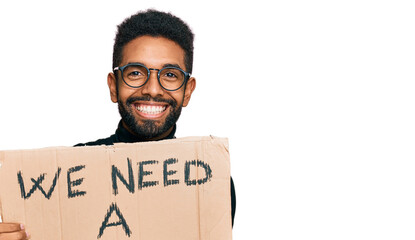 Young african american man holding we need a change banner celebrating victory with happy smile and winner expression with raised hands