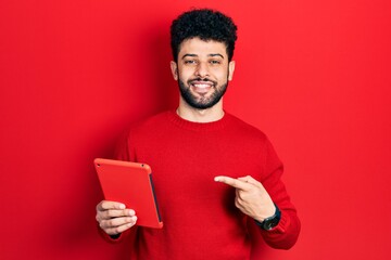 Young arab man with beard using touchpad device smiling happy pointing with hand and finger