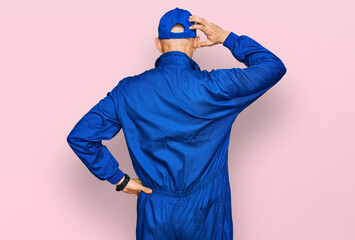 Bald man with beard wearing builder jumpsuit uniform backwards thinking about doubt with hand on...
