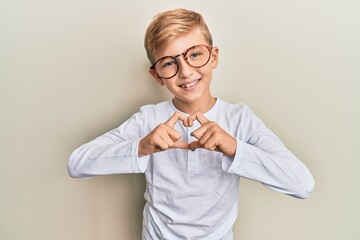 Little caucasian boy kid wearing casual clothes and glasses smiling in love doing heart symbol shape with hands. romantic concept.