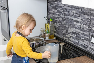 Naklejka premium Cute little boy is holding a measuring cup for water in the kitchen. Horizontally. 