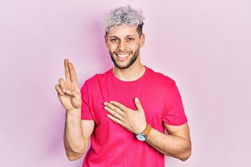Young hispanic man with modern dyed hair wearing casual pink t shirt smiling swearing with hand on...