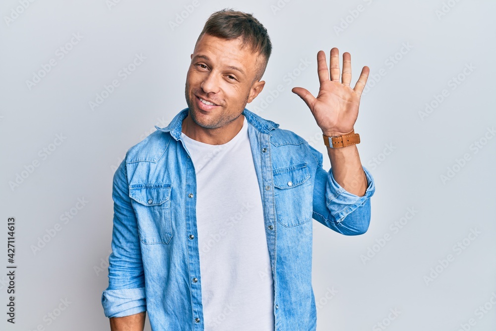 Sticker Handsome muscle man wearing casual denim jacket showing and pointing up with fingers number five while smiling confident and happy.