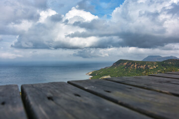 Scenic shot from wooden table over valley with sea view and rain clouds