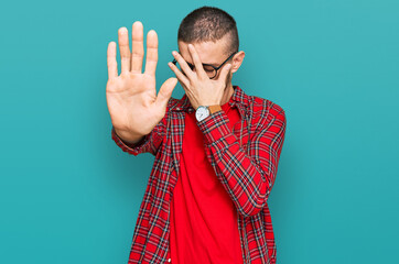 Hispanic young man wearing casual clothes covering eyes with hands and doing stop gesture with sad...
