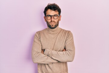 Handsome man with beard wearing turtleneck sweater and glasses skeptic and nervous, disapproving expression on face with crossed arms. negative person.