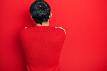 Handsome man with beard wearing casual red sweater hugging oneself happy and positive from...