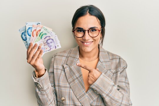 Young brunette woman holding singapore dollars banknotes smiling happy pointing with hand and finger