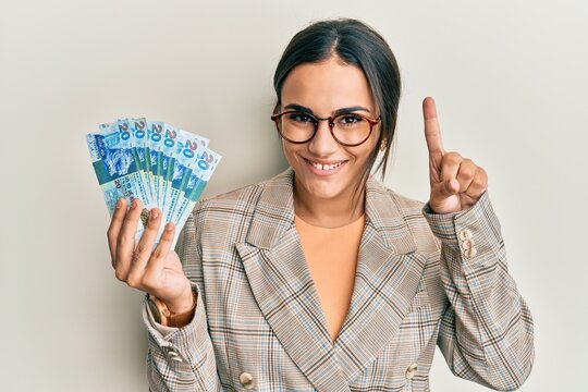 Young brunette woman holding hong kong 20 dollars banknotes smiling with an idea or question pointing finger with happy face, number one