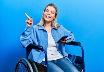 Beautiful caucasian woman sitting on wheelchair using smartphone smiling happy pointing with hand...