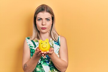 Beautiful caucasian woman holding piggy bank skeptic and nervous, frowning upset because of problem. negative person.