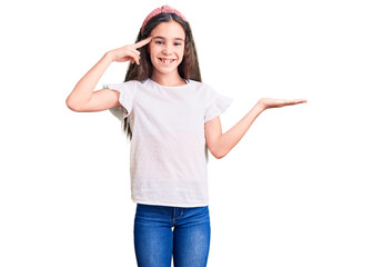 Cute hispanic child girl wearing casual white tshirt confused and annoyed with open palm showing copy space and pointing finger to forehead. think about it.