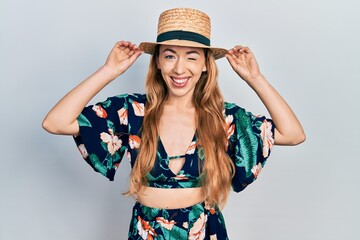 Young caucasian woman wearing summer hat winking looking at the camera with sexy expression,...