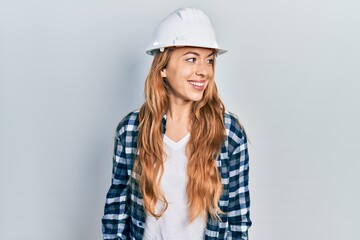 Young caucasian woman wearing architect hardhat looking away to side with smile on face, natural expression. laughing confident.