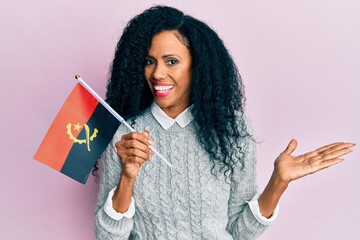 Middle age african american woman holding angola flag celebrating achievement with happy smile and winner expression with raised hand